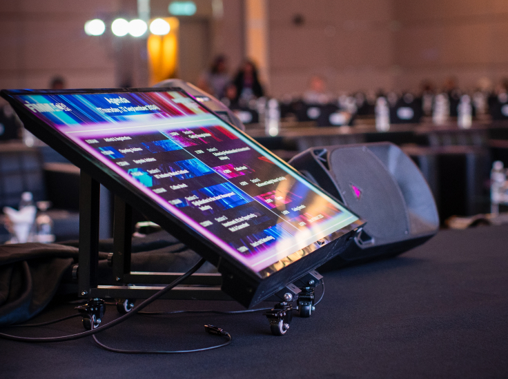 Large angled stage TV teleprompter displaying colorful text at an event.